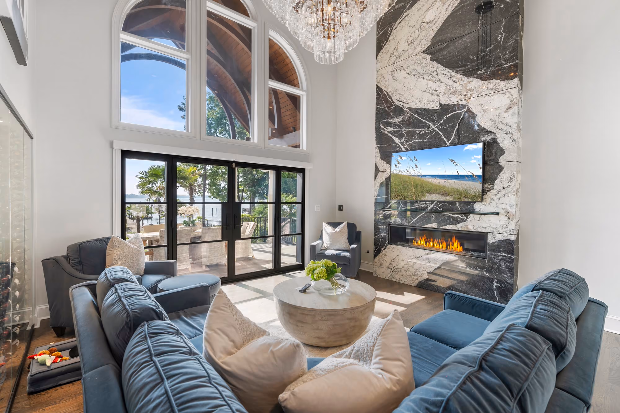 A two storey living room with a marble fireplace wall and glass doors onto the water.