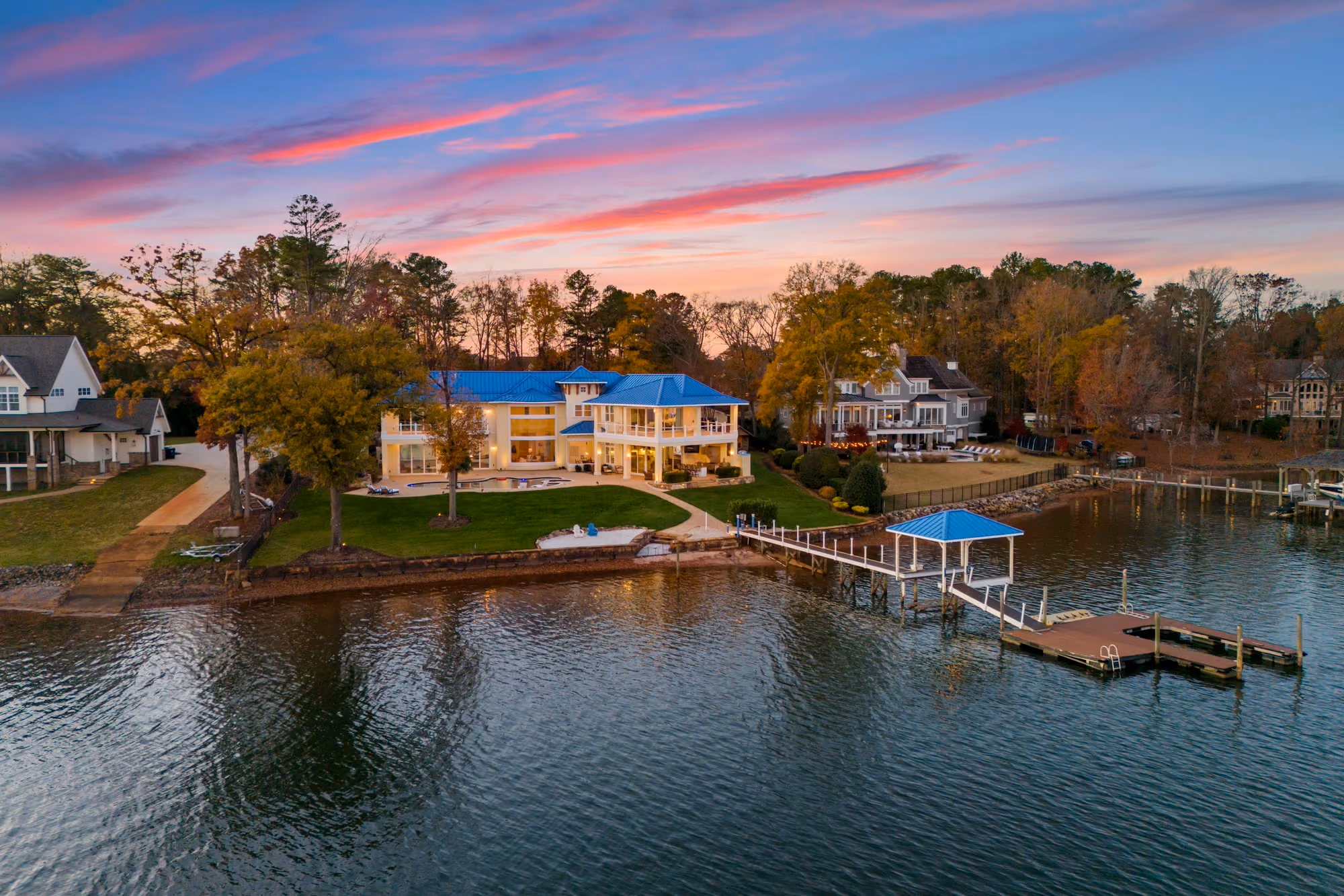 A lit house and its covered dock, seen across the water at dusk.