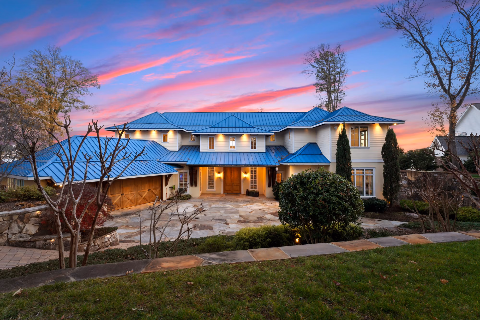 A blue roofed house with every window lit under a pink sky.