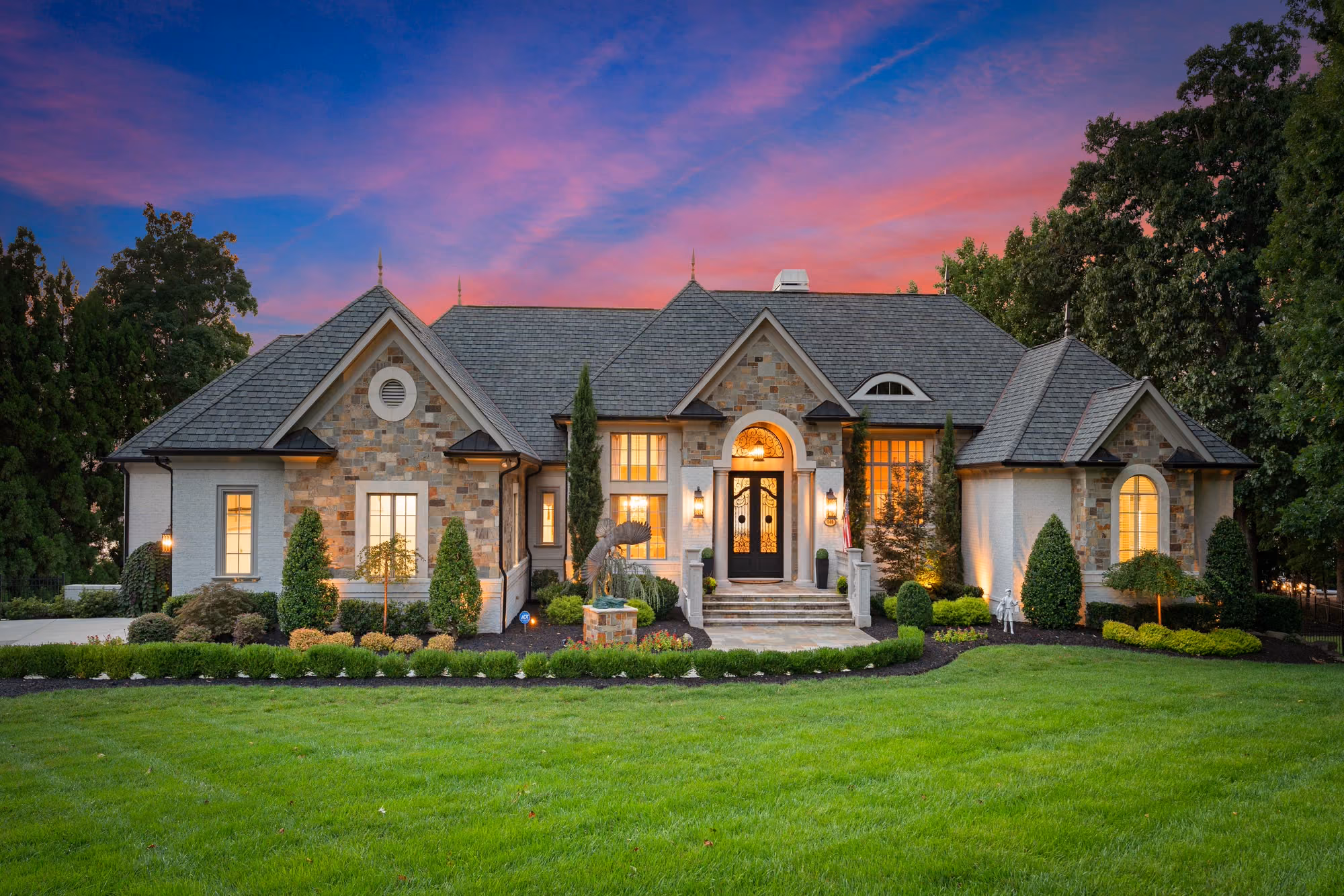 A stone and shingle entry lit at dusk, with a pink sky behind the roofline.
