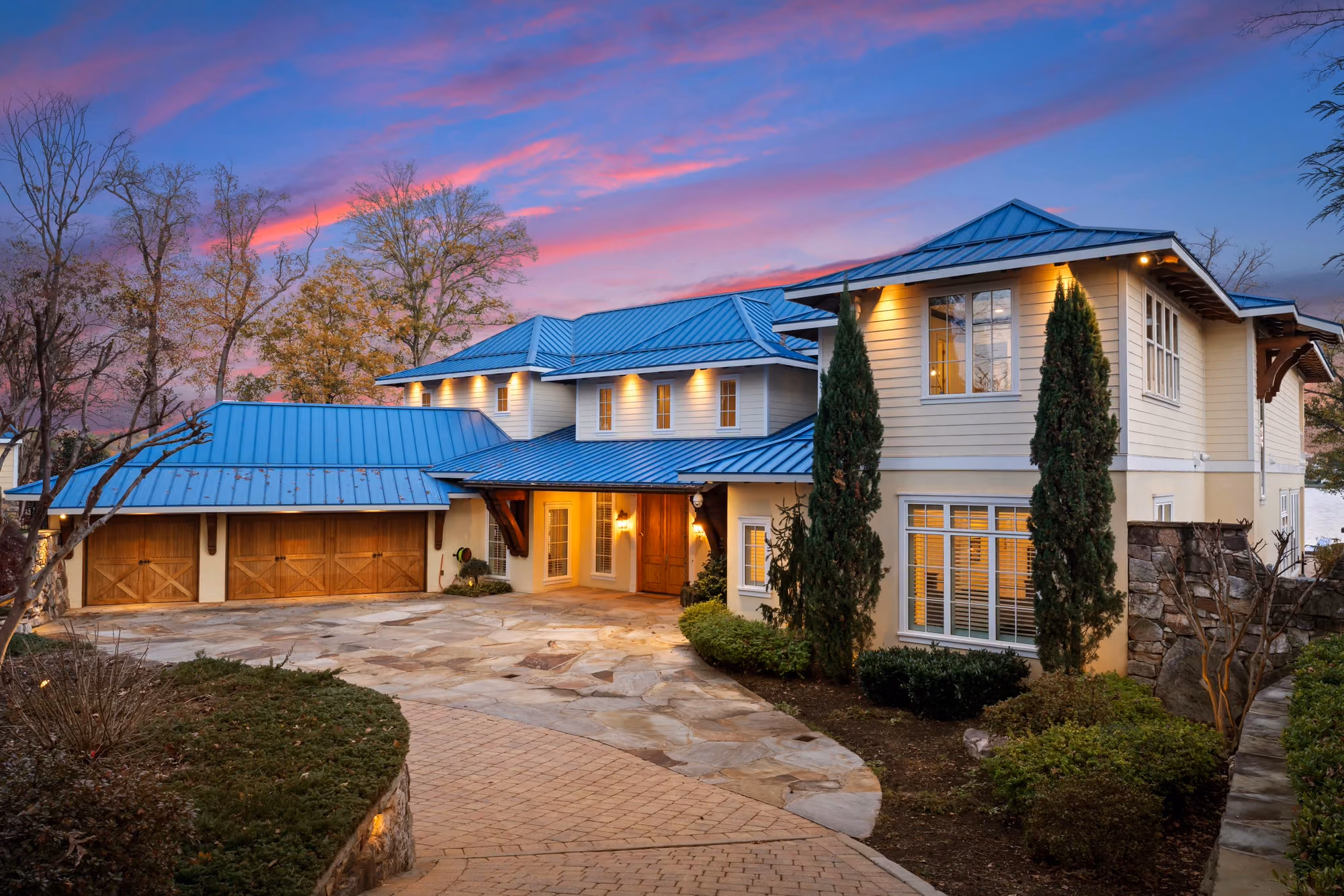 A paved motor court running up to a lit house under a pink evening sky.