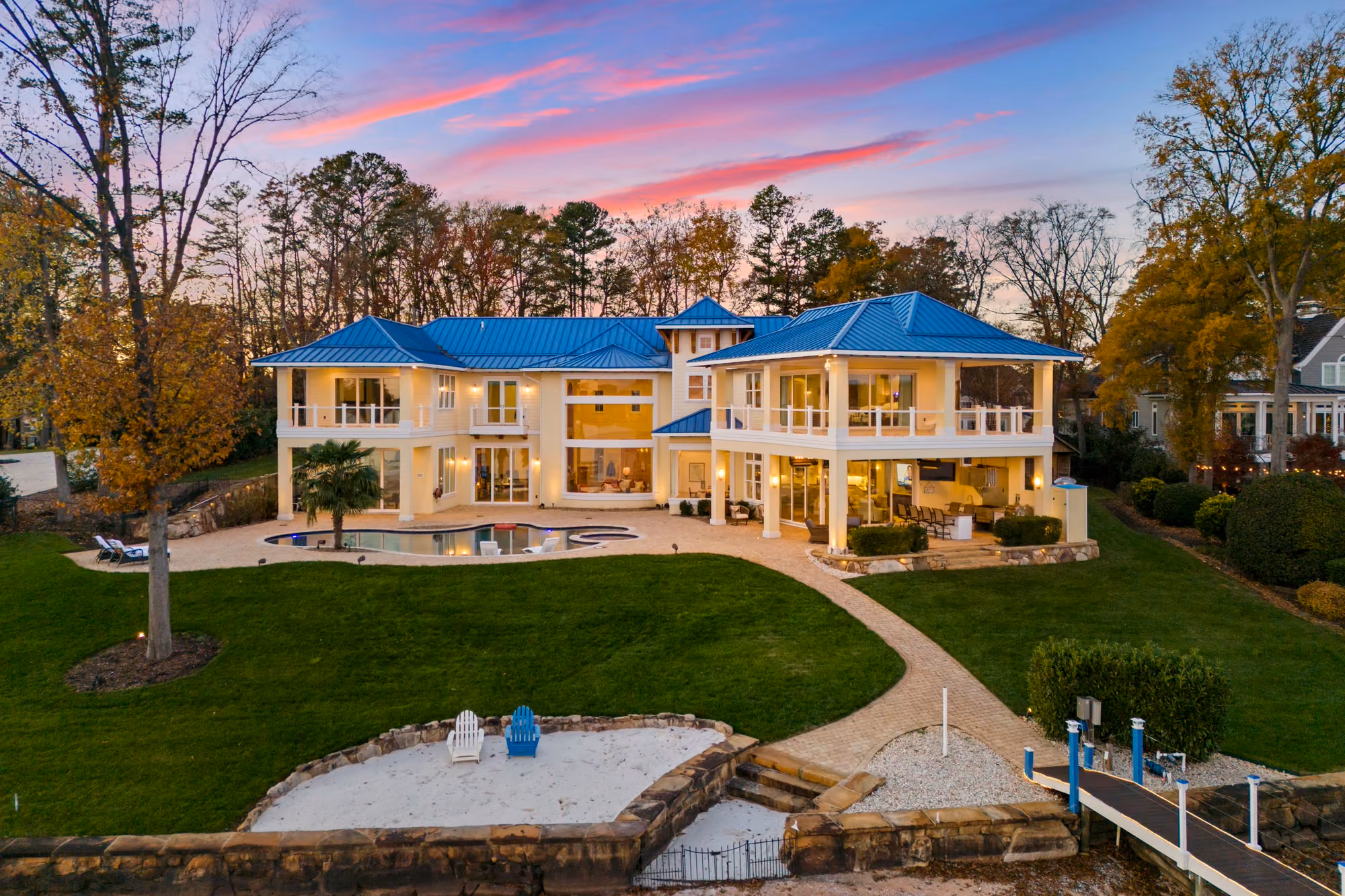 A lit house above its pool and its shoreline at dusk, from the air.