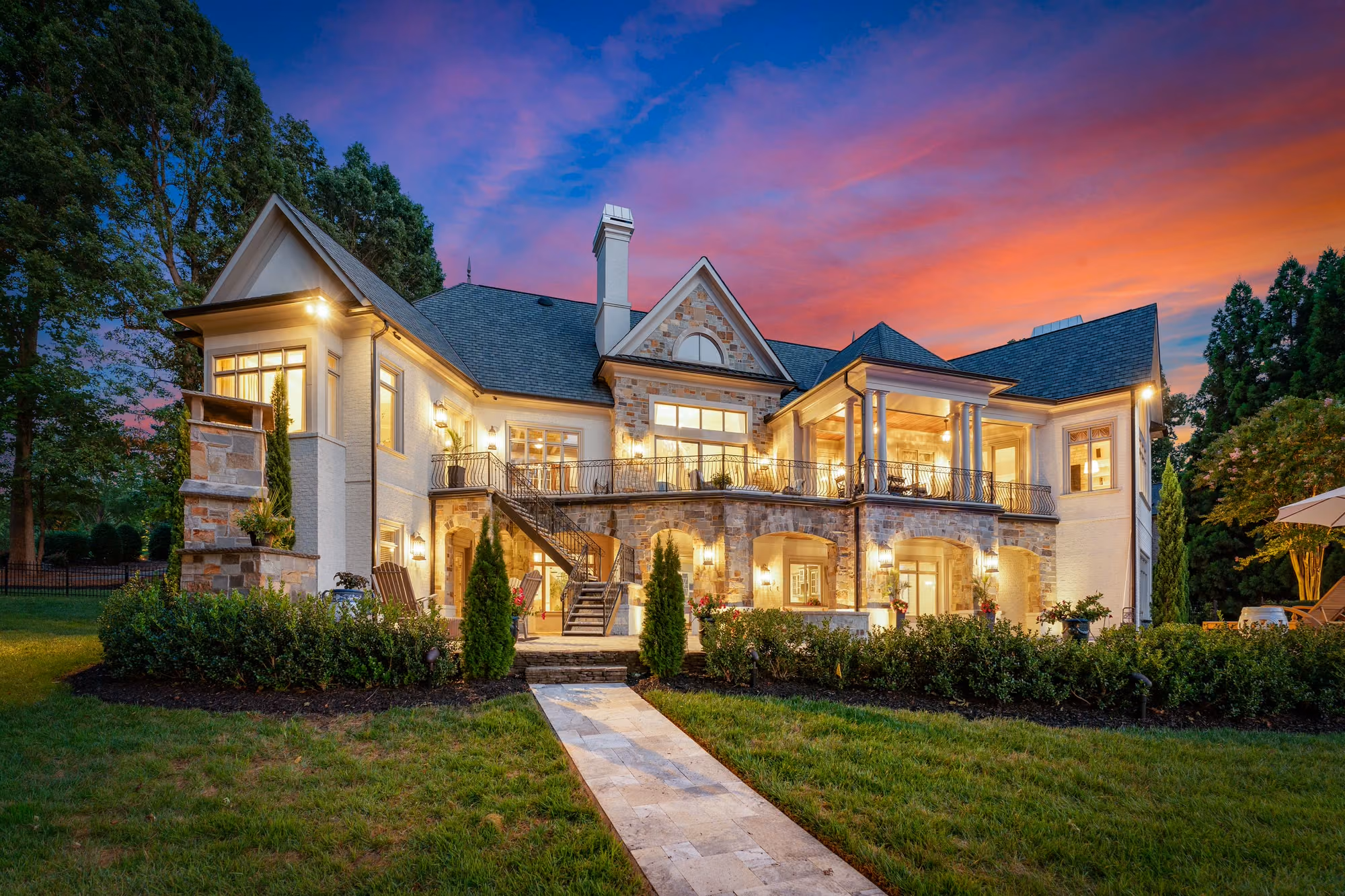 The back of a stone house at dusk, its balconies and windows lit.