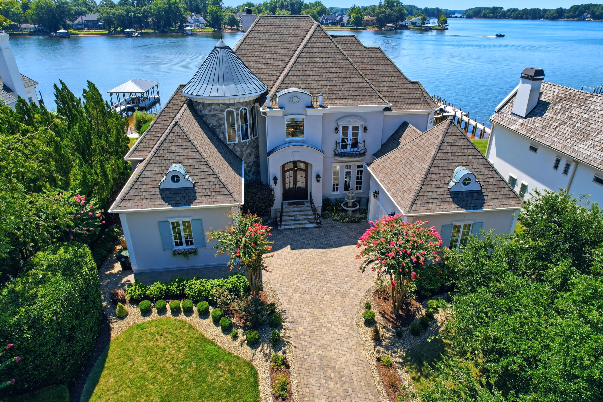 A turreted stucco house and its drive from the air, with the lake behind.