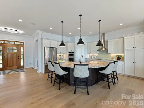 Gourmet chef's kitchen features an oversized quartz island with seating, custom cabinetry, stainless steel appliances, subway tile backsplash, and seamless flow into the dining and living areas, making it ideal for entertaining.