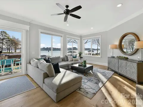Inviting Great Room showcases a striking floor-to-ceiling stone fireplace, expansive windows with stunning Lake Norman views, and seamless access to the outdoor living spaces.