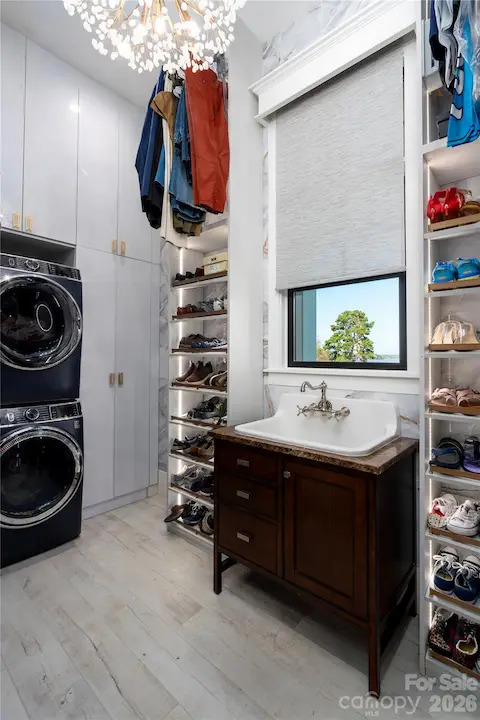 ULTRA-LUXURY LAUNDRY DESIGNED FOR ULTIMATE ORGANIZATION. FEATURING PREMIUM FRONT-LOAD WASHER AND DRYER SET, AN ELEGANT DARK WOOD VANITY WITH A DEEP FARMHOUSE-STYLE UTILITY SINK, FLOATING CHANDELIER WITH MOTORIZED LIFT FOR EASY MAINTENANCE, AND COMPREHENSIVE CUSTOM BUILT-IN STORAGE WITH FLOOR-TO-CEILING SHELVING FOR SHOES AND CLOTHING, MOTORIZED HANGING BARS ACCOMMODATES EFFORTLESS ACCESS!