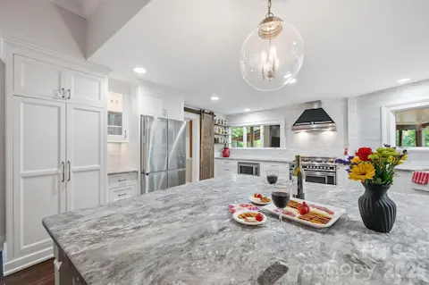 Pantry Wall with pull out shelves, glass display cabinets with under counter lighting, large dining & entertaining island.  Countertop to ceiling tiled accent wall