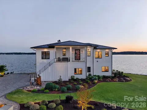 STUNNING LAKEFRONT CURB APPEAL, THIS COASTAL MODERN CRAFTSMAN ESTATE FEATURES CRISP WHITE BOARD-AND-BATTEN SIDING, CONTRASTING DARK TRIM, PREMIUM STANDING SEAM METAL ROOF AND AN ELEGANT EXTERIOR STAIRCASE.  PERFECTLY COMPLEMENTED BY METICULOUSLY DESIGNED PROFESSIONAL LANDSCAPING AND EXPANSIVE PAVER DRIVEWAY