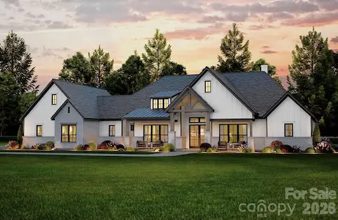 This stunning modern farmhouse features a crisp white exterior with board-and-batten siding, contrasting dark trim, and a welcoming covered front porch accented by timber beams and brick columns.