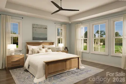 This spacious primary bedroom features a tray ceiling and expansive windows that flood the room with natural light and frame serene outdoor views.