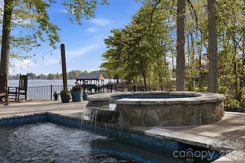 In-ground pool and spa with waterfall feature overlook a spacious patio and scenic water views.