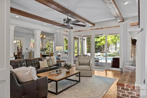 Light-filled living area with exposed ceiling beams, fireplace, and large sliding doors opening to a covered patio and pool.