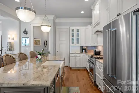 Kitchen features a large island with seating, farmhouse sink, custom cabinetry, stainless steel appliances, and ample counter space.