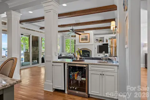 Wet bar with beverage refrigerator and sink overlooks the living area with exposed beams and fireplace.