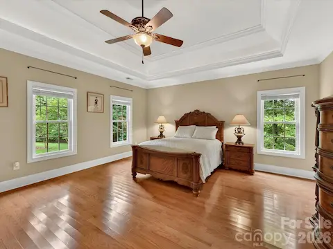 Spacious primary suite features hardwood floors, elegant tray ceilings, abundant natural light, and a peaceful retreat-like atmosphere.