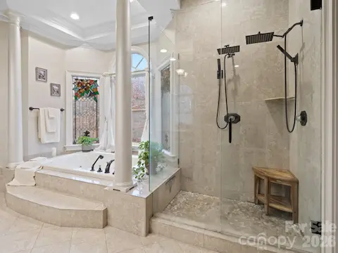 In the primary bath, you’ll find a spacious tile shower with dual heads, a soaking tub accented by graceful columns, and a double vanity with custom cabinets.