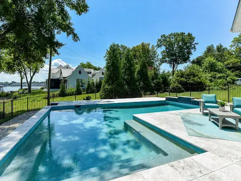 Resort-style saltwater pool with expansive travertine decking creates a stunning outdoor retreat overlooking serene waterfront views, perfect for relaxing and entertaining.