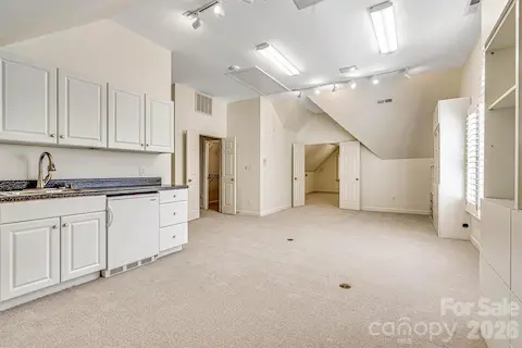 Expansive bonus room with french doors,  neutral carpet, custom built-ins & wet bar with beverage fridge, sink and added overhead cabinetry.