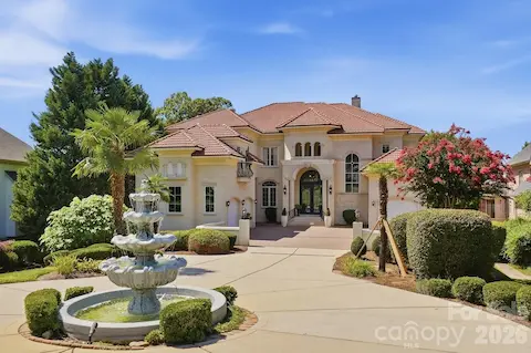 A beautifully landscaped circular drive welcomes you with a tiered fountain as its centerpiece, surrounded by mature palms, sculpted hedges, flowering trees, and manicured plantings. The lush grounds soften the approach and create a private, resort-like setting, while the broad driveway offers an elegant and memorable arrival experience.