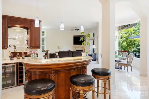 A true showpiece for entertaining, the custom curved bar features a striking backlit onyx countertop that creates a warm, dramatic glow and highlights the stone’s natural veining. Rich wood cabinetry, glass display shelving, beverage refrigeration, pendant lighting, and bar seating complete this sophisticated gathering space, which flows effortlessly into the adjacent sitting and outdoor living areas.