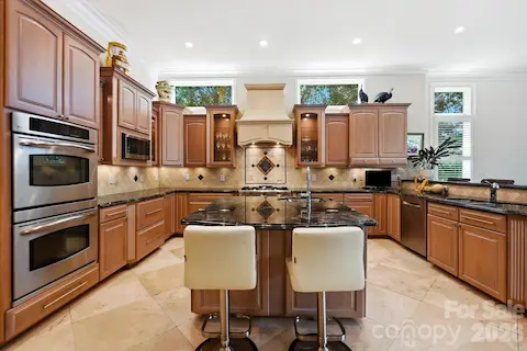 Continuing from the entertaining areas, the spacious kitchen blends warmth and function with rich custom cabinetry, expansive stone countertops, and a large center island with additional seating. Stainless-steel appliances, decorative tilework, abundant storage, and generous prep space make this a beautifully equipped centerpiece for both everyday living and entertaining.