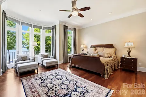 The spacious primary suite offers a serene waterfront retreat, with rich hardwood flooring, a private fireplace, and a sitting area positioned to enjoy beautiful views of Lake Norman through a wall of windows.