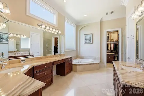 The adjoining primary bath is generously sized and thoughtfully designed with dual vanities, extensive cabinetry, expansive stone countertops, a soaking tub, and a separate glass-enclosed shower. High ceilings and abundant natural light enhance the spa-like atmosphere.