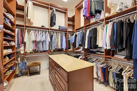 Completing the primary suite, the large walk-in closet features extensive custom wood built-ins with multiple hanging areas, open shelving, shoe storage, and a center island with drawers—providing exceptional organization and storage.