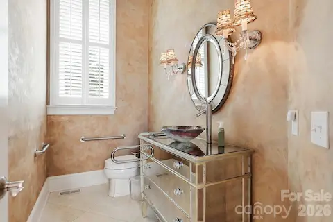 A stylish powder room adds a distinctive touch with a vessel sink, mirrored vanity, decorative sconces, and softly textured walls, while the window brings in natural light.
