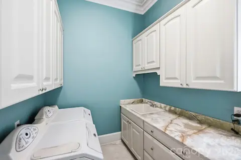 The dedicated laundry room combines practicality with generous storage, featuring extensive cabinetry, a utility sink, and a long stone countertop that provides ample folding and workspace.