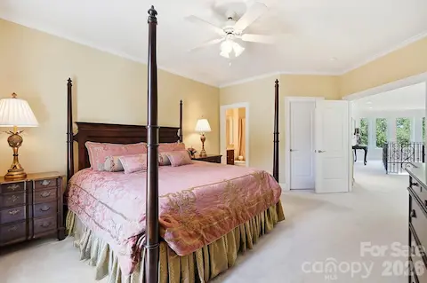 This spacious secondary bedroom offers a comfortable private retreat with generous proportions, crown molding, a ceiling fan, and direct access to its own en suite bath. The open doorway also provides a glimpse back toward the upper gallery and central staircase.