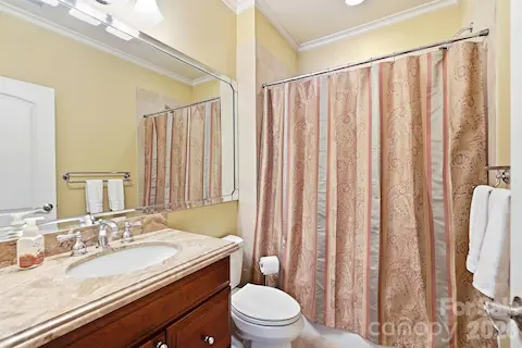 The adjoining bath features a stone-topped vanity, large mirror, tub/shower combination, and classic finishes, giving overnight guests or family members a convenient and comfortable stay.