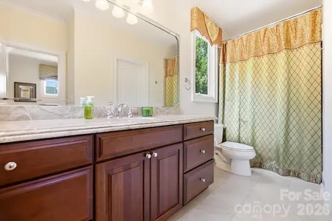 Nearby, a well-appointed full bath features a long stone-topped vanity with rich wood cabinetry, a tub/shower combination, and a window for natural light, providing comfortable accommodations for the adjoining upper-level rooms.