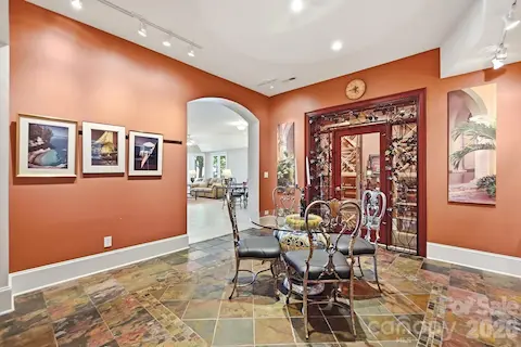 The lower level opens to a distinctive gallery-style entertaining space with richly colored slate flooring, track lighting for artwork, and generous room for dining, games, or casual gatherings. The back staircase provides easy access to the levels above.