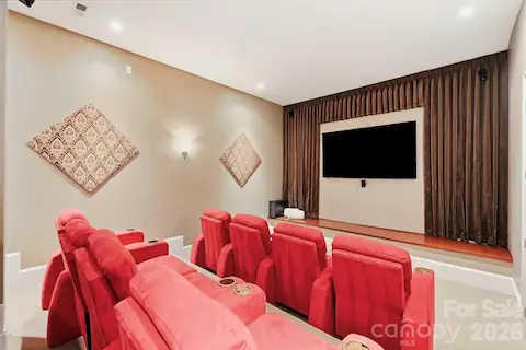 Creatively connected to the lower-level entertaining area is a home theater designed for movie nights and game days with tiered seating, multiple theater-style recliners, a large screen, and integrated speakers for an immersive entertainment experience.