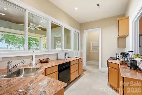 The lower level includes a convenient secondary kitchenette with granite countertops, ample cabinetry, a sink, dishwasher, and additional prep space. Large interior windows maintain the connection to the covered lakeside living areas beyond.