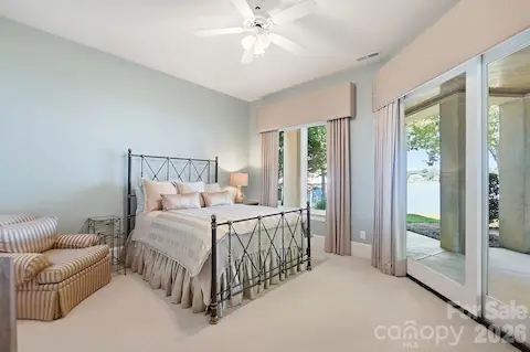 A comfortable guest bedroom offers direct access to the covered patio and beautiful Lake Norman views, creating a private retreat for overnight visitors. Soft carpeting, generous windows, and space for a sitting area enhance the room’s relaxed feel.
