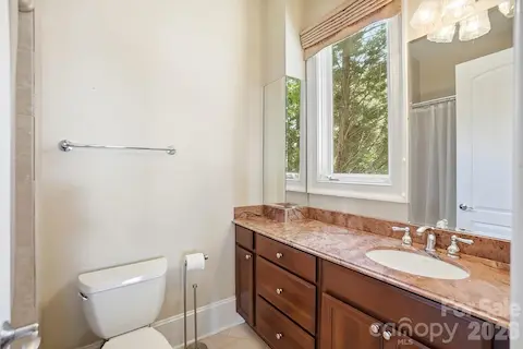 The adjoining bath features a stone-topped vanity, rich wood cabinetry, tub/shower combination, and a window overlooking the surrounding greenery, providing convenient accommodations for the lower-level guest suite.