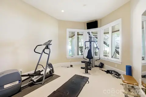 The dedicated fitness room offers generous space for cardio and strength-training equipment, with multiple windows bringing in natural light and views toward the lake. Its lower-level location creates a convenient private workout space just steps from the outdoor waterfront areas.