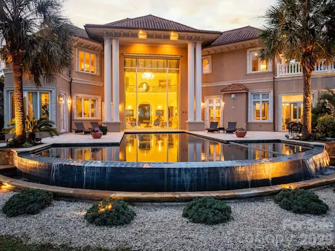 A stunning nighttime view looking back at the home and expansive pool, showcasing the property’s impressive outdoor living and waterfront setting.