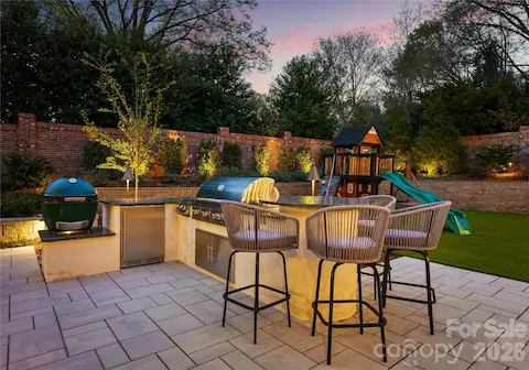 Outdoor kitchen with gas grill, gas cooktop, Big Green Egg, beverage fridge, and bar seating for 4.
