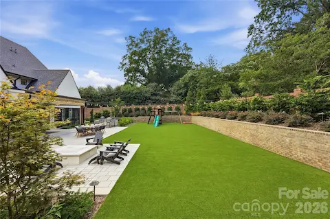 Large turf lawn with lots of mature plantings and brick privacy wall.