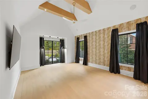 Primary bedroom with custom blackout draperies, vaulted ceiling with beams, and a large window overlooking the backyard.