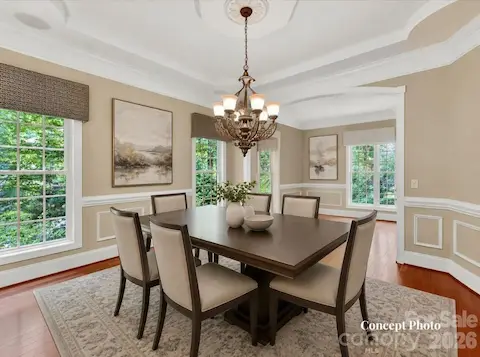 Concept photo of virtually staged elegant formal dining room features extensive crown molding, tray ceiling details, hardwood floors, and seamless flow into the adjoining living spaces for effortless entertaining.
