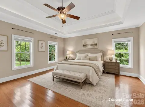 Concept photo of virtually staged spacious primary suite features hardwood floors, elegant tray ceilings, abundant natural light, and a peaceful retreat-like atmosphere.