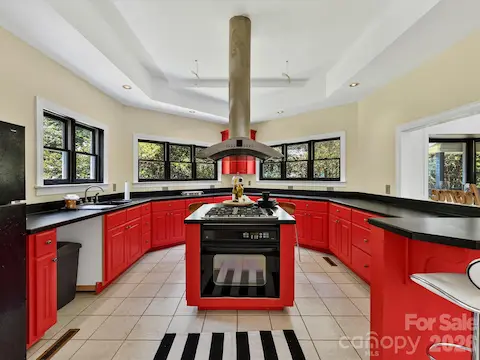 Spacious kitchen offers tile flooring, abundant cabinetry and counter space, a center island with cooktop, and windows overlooking the wooded property.