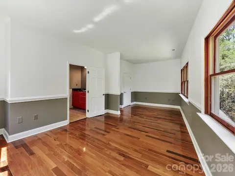Spacious primary suite features gleaming Brazilian hardwood floors, abundant natural light, and peaceful wooded views from multiple oversized windows.