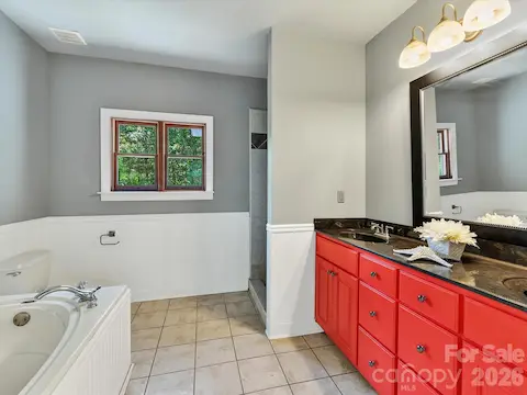 Primary bath features tile flooring, a soaking tub, separate shower, spacious vanity, and natural light from a wooded-view window.