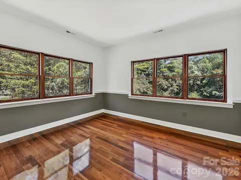 Bright secondary bedroom showcases Brazilian hardwood floors, multiple windows, and serene views of the surrounding Davidson woods.